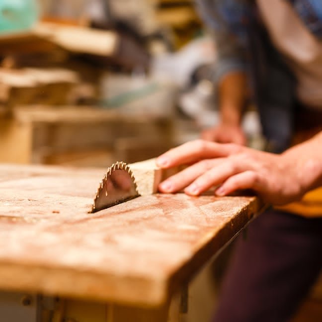 Close-up of a hand guiding a board through a table saw during a precision cut