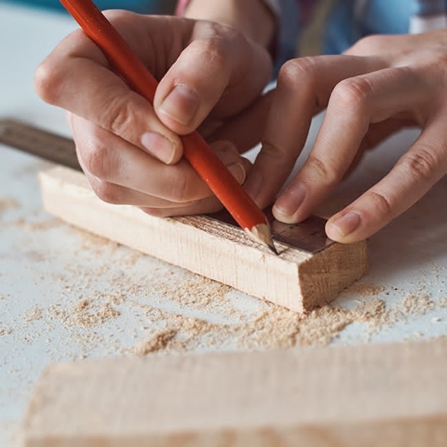 Carpenter marking precise measurements on a board with a pencil during the planning stage